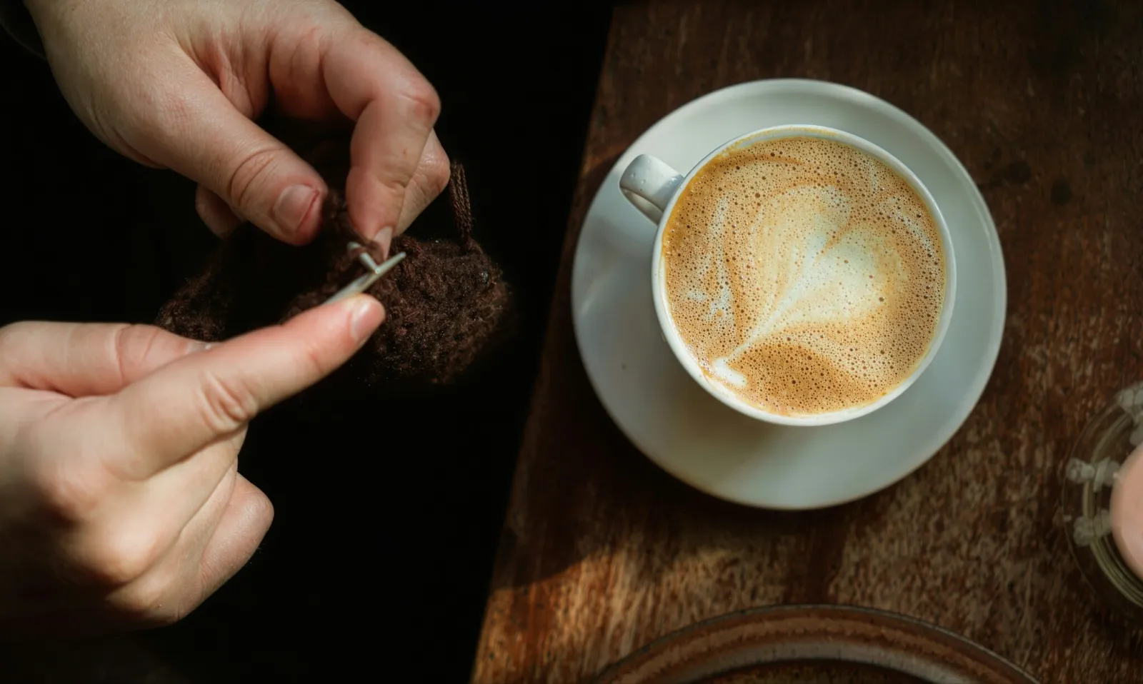 Hands knitting brown wool beside a latte on a wooden table